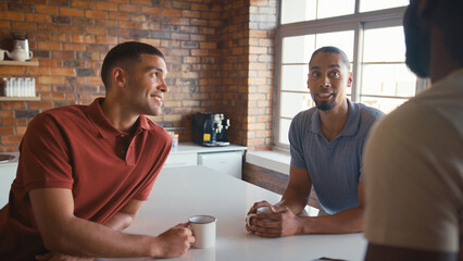 Multi-Cultural Businessmen Taking Coffee Break In Kitchen Area Of Modern Open Plan Office Together