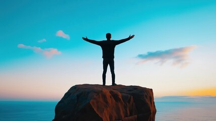 Man standing triumphantly on mountain peak at sunrise
