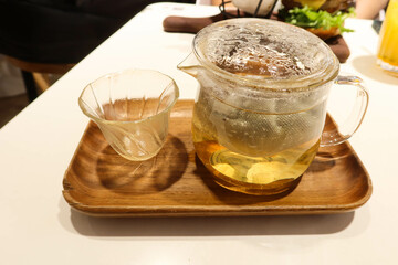 close up of a hot pot of jasmine tea in a glass pot, a glass up on a wooden tray placed on a white table in a cafe