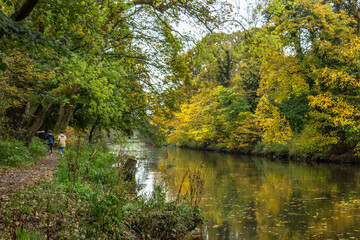 Two young women enjoying a fine autumn day with a walk along the path beside the River Aire in Hirst Wood with the colourful leaves reflected in the water