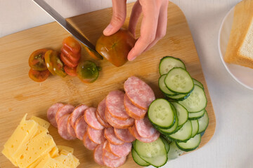 Woman cooking cutting tomatoes on thin slices using knife on wooden board. Hands of woman cook sandwiches on kitchen at home. Meat delicacy for cooking pizza, other dishes. Preparing snack food.