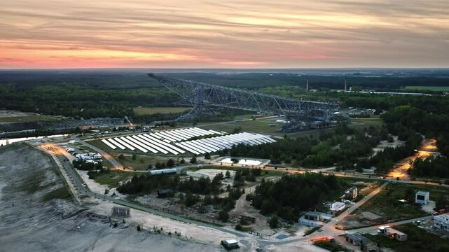 F60 Drone video of a giant excavator bridge silhouetted against a sunset. The sun sets behind the massive structure, highlighting the scale and industrial atmosphere. Drone move forward