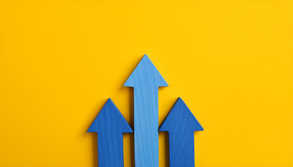 Blue wooden arrow pointing upwards on yellow background. Business and market growth. Flat lay