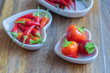 three heart shaped plate full of fresh hot peppers on wooden background