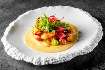 A close-up of a gourmet dish featuring a puree with diced seafood and garnished with fresh herbs, served on an elegant white plate against a dark background