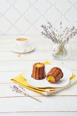 Dessert, canele with lemon curd on a white plate on a light wooden background.