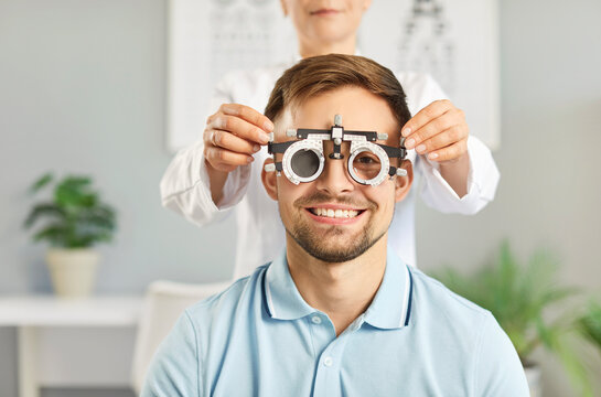 Happy, smiling male patient getting eye check at optometrist's office. Optometrist uses specialized ophthalmic equipment to test eyesight of young man who needs prescription glasses. Optometry concept