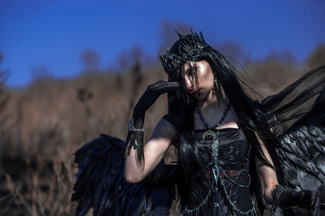 Obraz premium Goddess of death with black wings on a dried field
