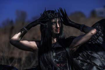 Naklejka premium Goddess of death with black wings on a dried field