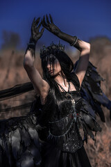 Naklejka premium Goddess of death with black wings on a dried field