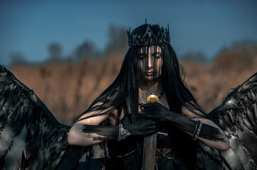 Obraz premium Goddess of death with black wings on a dried field