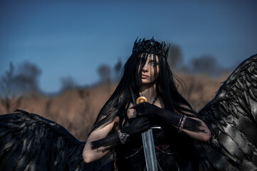 Goddess of death with black wings on a dried field