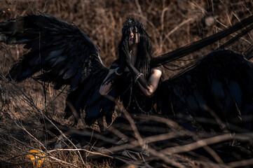 Goddess of death with black wings on a dried field