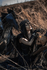 Naklejka premium Goddess of death with black wings on a dried field