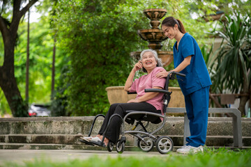 Elderly woman seated in a wheelchair with young caregiver or healthcare worker is standing behind  reflects care, compassion, and a supportive relationship the caregiver and  elder healthy concept.