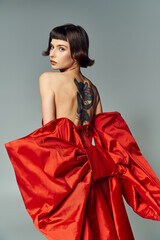 A stylish woman showcases her unique tattoo while posing gracefully in a vibrant dress.