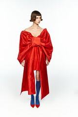 A fashionable young woman poses elegantly in a vivid red dress with a large bow.