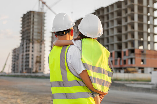 Portrait of a father and daughter in protective helmets on the background of a construction site.