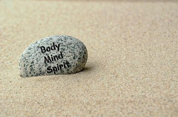 Body, Mind and Spirit text on zen stone buried in the sand.