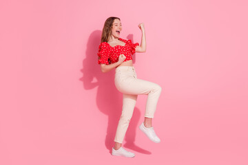 Full body photo of attractive teen woman raise fists winning dressed stylish red clothes isolated on pink color background