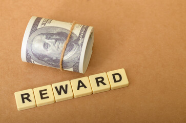 The image visually represents the concept of a reward, with the word "REWARD" spelled out in tiles and accompanied by a roll of money.