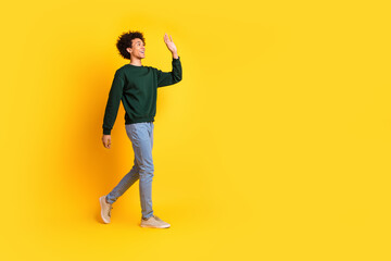 Full body portrait of nice young man walk wave empty space wear sweater isolated on yellow color background