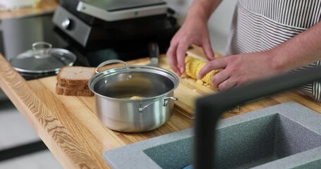 Male hands put pieces of chopped corns into saucepan at wooden countertop in kitchen slow motion. Man in apron prepares ingredients for cooking boiled cob - Powered by Adobe
