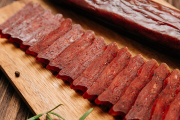 Sliced gourmet smoked salami on a wooden board with herbs, perfect for charcuterie boards and snacks