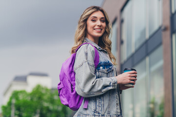 Profile portrait of pretty young girl backpack coffee cup wear denim jacket walk street outdoors