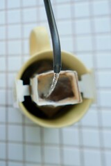 yellow cup freshly brewed coffee with convenient drip filter on kitchen table. prepare freshly brewed coffee at home. Space place for text. concept of making hot drink. bag of drip coffee beans.