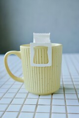 yellow cup freshly brewed coffee with convenient drip filter on kitchen table. prepare freshly brewed coffee at home. Space place for text. concept of making hot drink. bag of drip coffee beans.