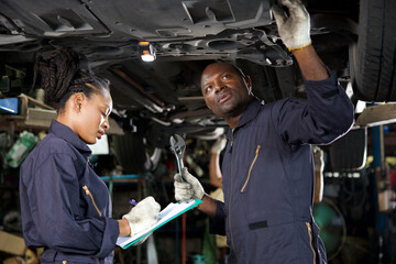 African mechanic workers fixing underneath car and talking about work in garage