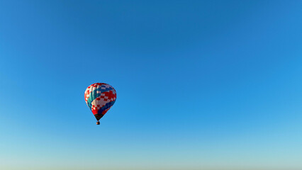 A vibrant hot air balloon glides gracefully across the expansive blue sky, enjoying a calm morning, highlighting the beauty of peaceful aerial adventures.
