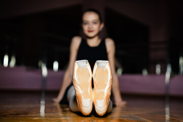 Young ballet dancer showcases worn shoes in rehearsal space. A young ballet dancer poses with her...