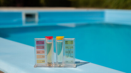 A pool water testing kit with pH and chlorine levels is placed on the pool's edge, with the blue...