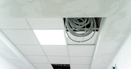Ceiling repair process showing exposed wiring in a commercial building. Ceiling tiles are removed, revealing wiring and unfinished repairs in a commercial space under renovation.