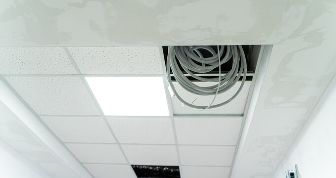 Ceiling repair process showing exposed wiring in a commercial building. Ceiling tiles are removed, revealing wiring and unfinished repairs in a commercial space under renovation.