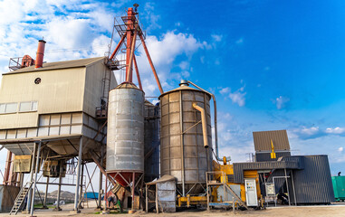 Industrial storage silos and processing equipment in bright daylight. Large silos and processing equipment stand against a clear blue sky