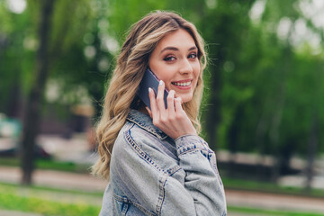 Profile photo of pretty young woman toothy smile speak phone wear denim jacket free time walk fresh air park outdoors