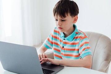 Boy schoolboy sitting at table with laptop online