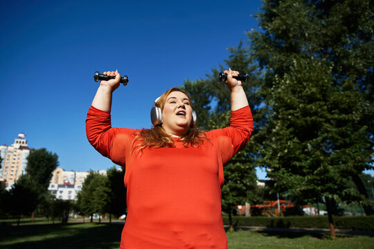Energetic plus size woman lifts dumbbells while enjoying a sunny day outdoors.