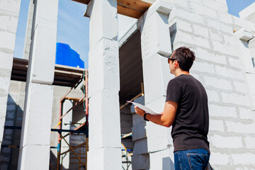 Man architect engineer checking house under construction comparing with blueprint plan on paper. Gas block