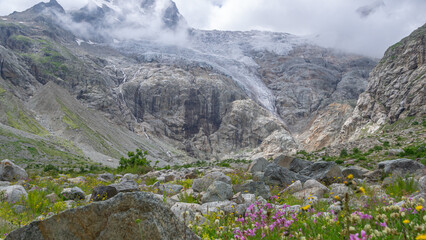 View of a glacier covered with clouds. Panorama in a mountain gorge. The glacier descends from the...