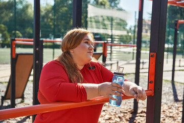 A woman pauses to hydrate during her workout in a vibrant park setting.