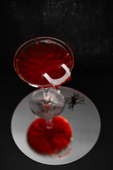 Vampire's Kiss Cocktail. Dracula's Blood Cocktail or Mocktail on dark background with reflection in mirror. Drink for Halloween with plastic vampire teeth as a garnish. Festive food and beverages.