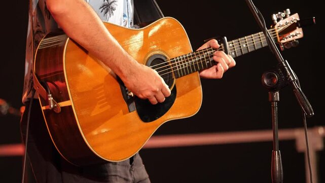 Close-up of a guitarist&rsquo;s hands energetically strumming the strings of his guitar. The stage lights create a vibrant atmosphere, enhancing the dynamic performance.