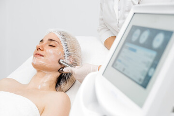 A cosmetologist applies radiofrequency lifting to a young woman in a modern clinic. This advanced...