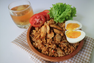 A plate of Nasi Goreng with rice, vegetables, sliced chicken and an boiled egg on top. Wooden plate.