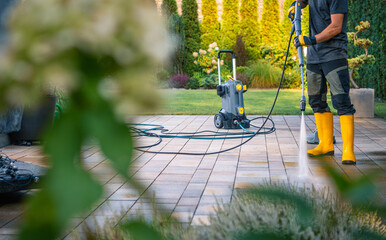 Man Cleaning Patio Tiles With a Pressure Washer in a Well-Maintained Garden on a Sunny Day