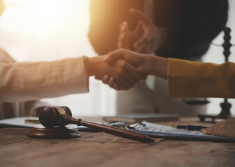Lawyer shaking hands with a client making about documents, contracts, agreements, cooperation agreements with a female client at the lawyer's desk and a hammer at the table.